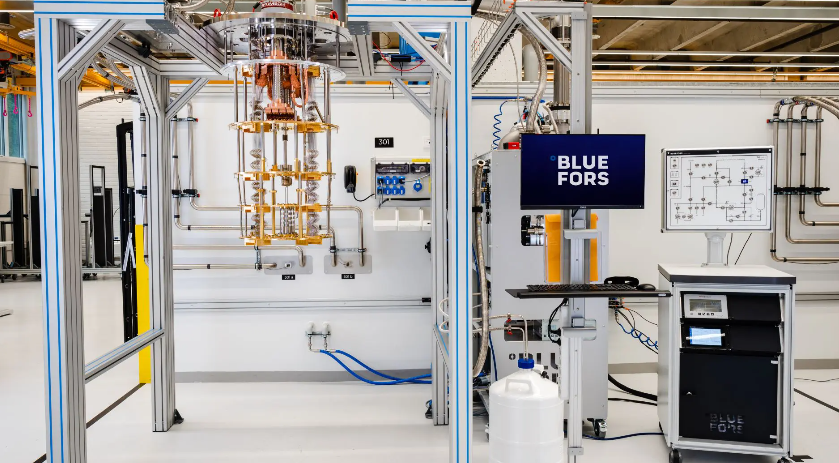 A commercial cryogen-free dilution refrigerator. The vertical stack contains the cooling stages from room temperature down to the millikelvin mixing chamber. The gas handling system and control electronics are on the right.